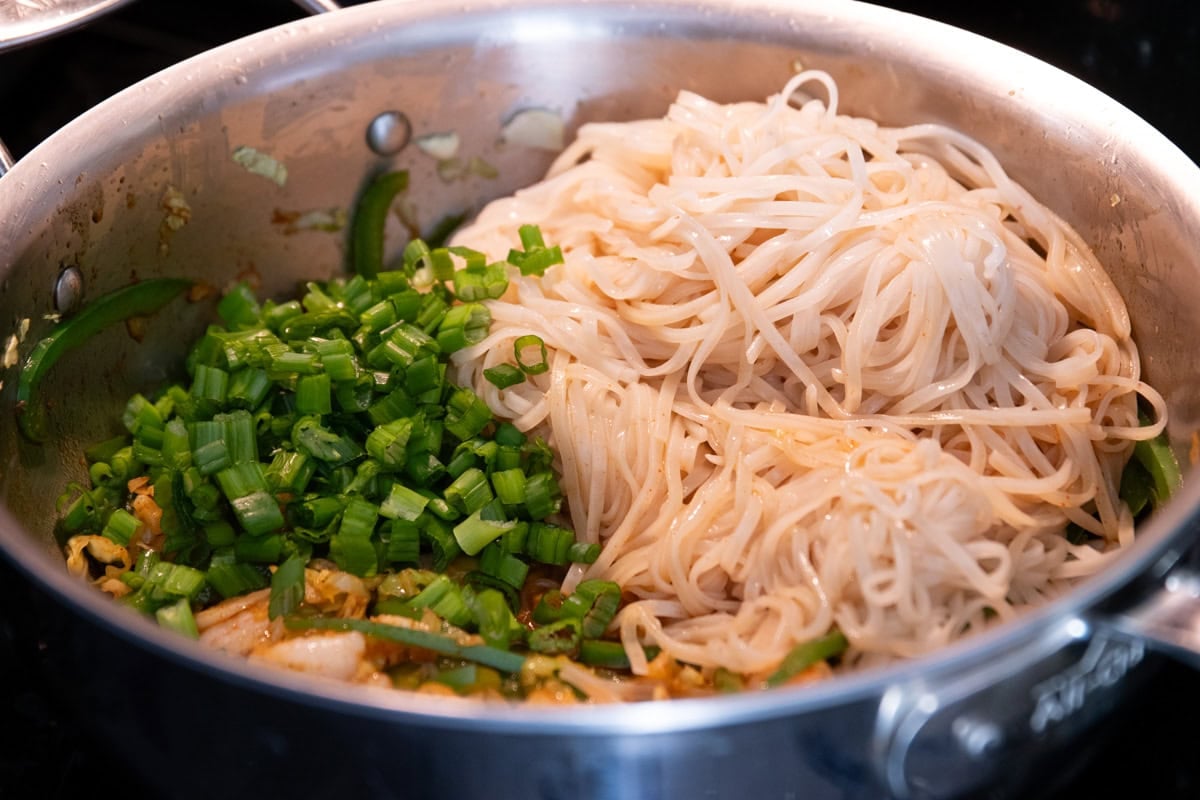 Cooked rice noodles and green onion tops have been added to the almost cooked shrimp, sauteed veggies and pad Thai sauce. 