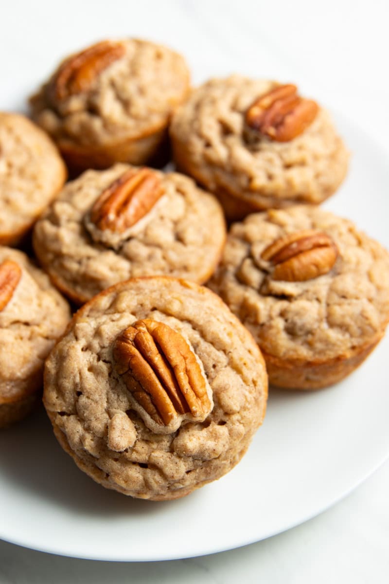 Close up of a pecan-topped oatmeal muffin on a plate filled with other, artistically blurred, muffins.