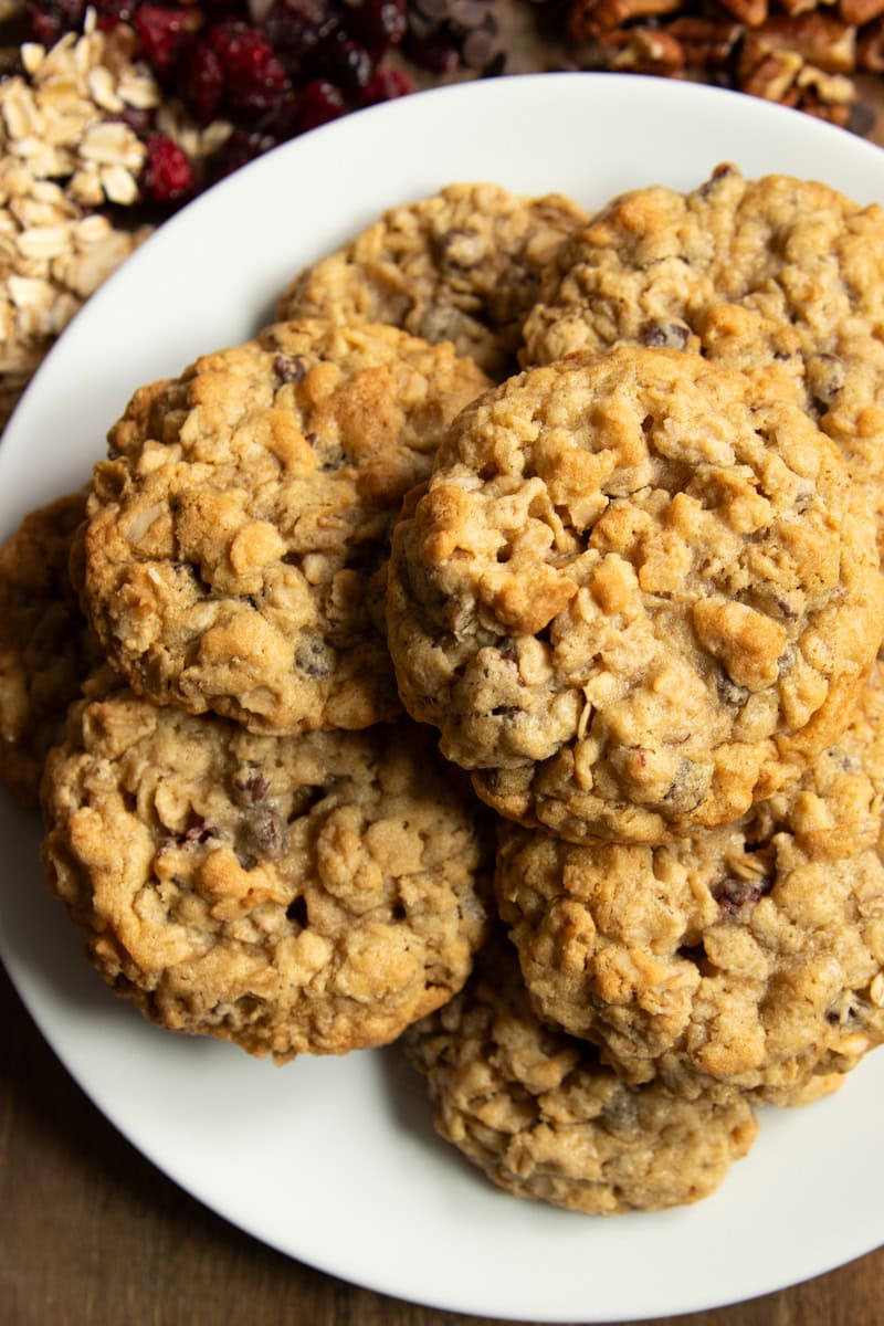 A plate of low FODMAP trail cookies surrounded by rolled oats, dried cranberries, chocolate chips, and pecans.