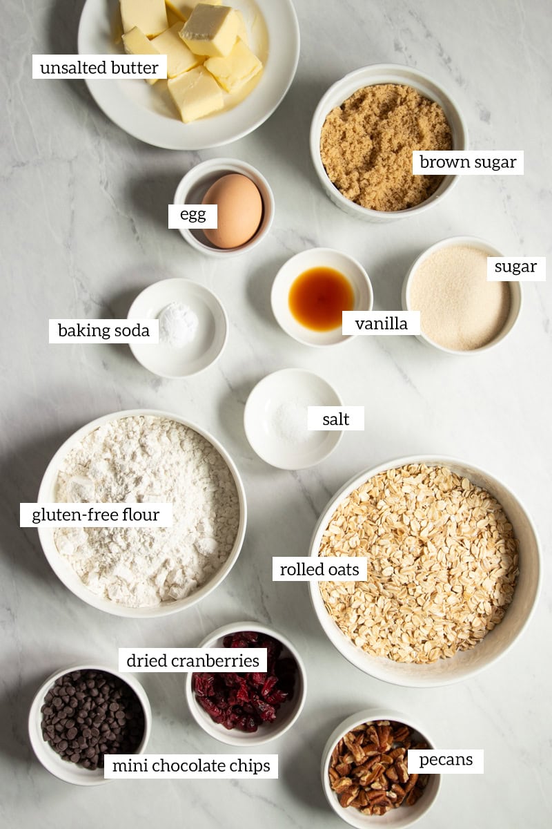 Ingredients needed to make low FODMAP trail cookies are measured out into individual containers on a white marble countertop.