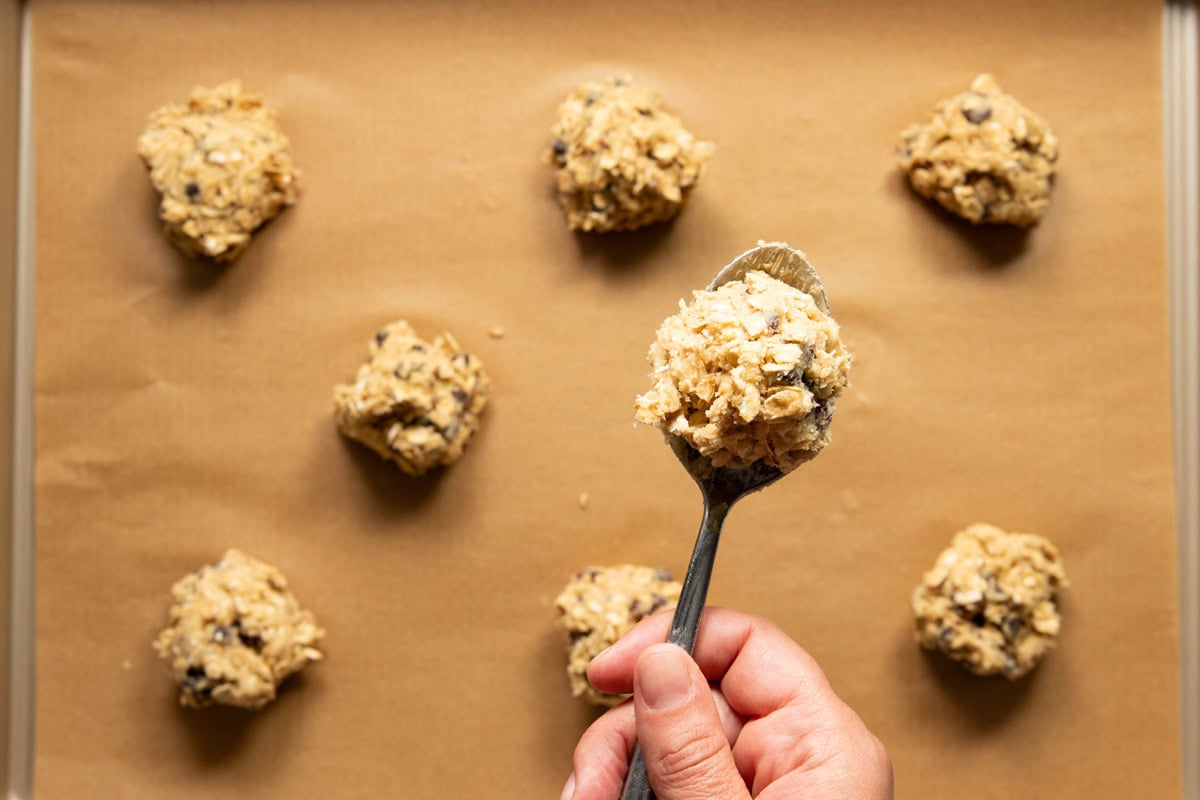 Scoop of cookie dough ready to join other cookie dough balls on a baking sheet lined with parchment paper.