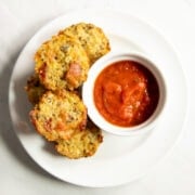 A small white plate filled with five low FODMAP pineapple bacon quinoa bites and a small dish of Fody Foods Tomato Basil Sauce.