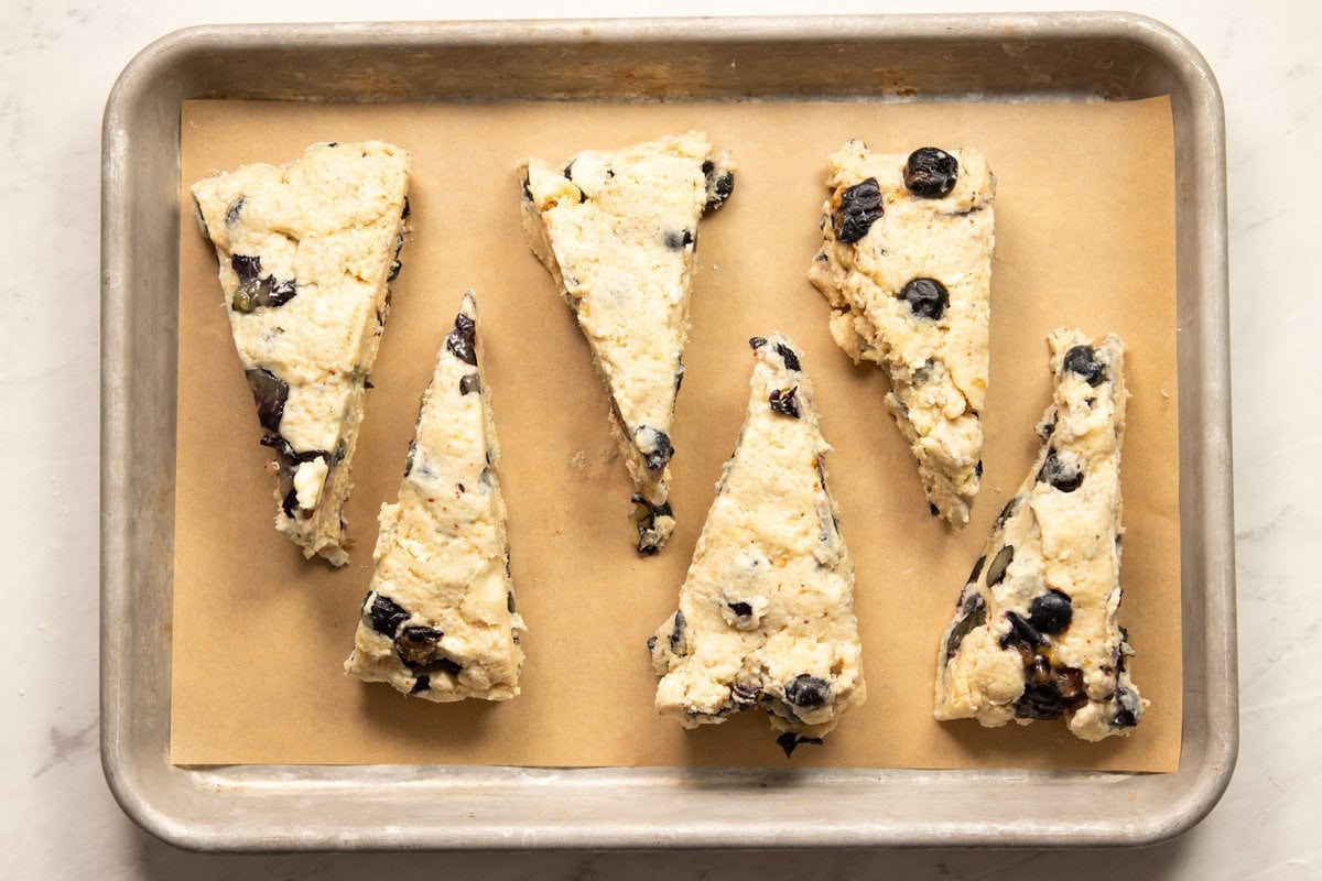 Six unbaked scone wedges are placed on a baking sheet lined with parchment paper - ready for baking.