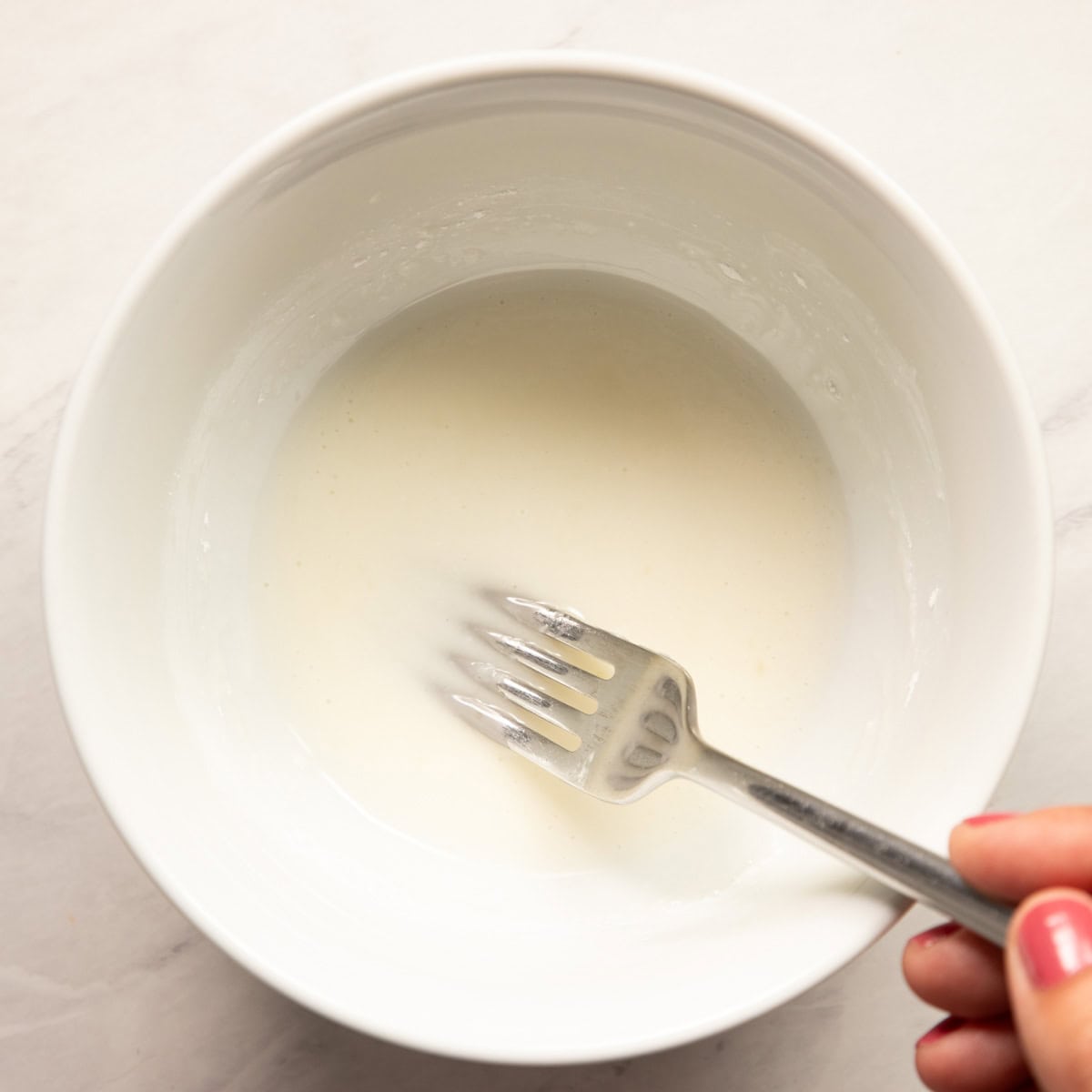 Whisking lemon juice and powdered sugar together in a small white bowl to make a lemon glaze. 