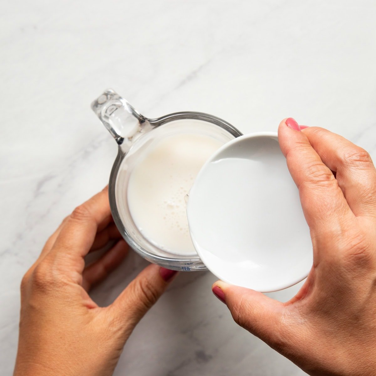 Pouring vinegar into a glass measuring cup of almond milk to make dairy-free "buttermilk"