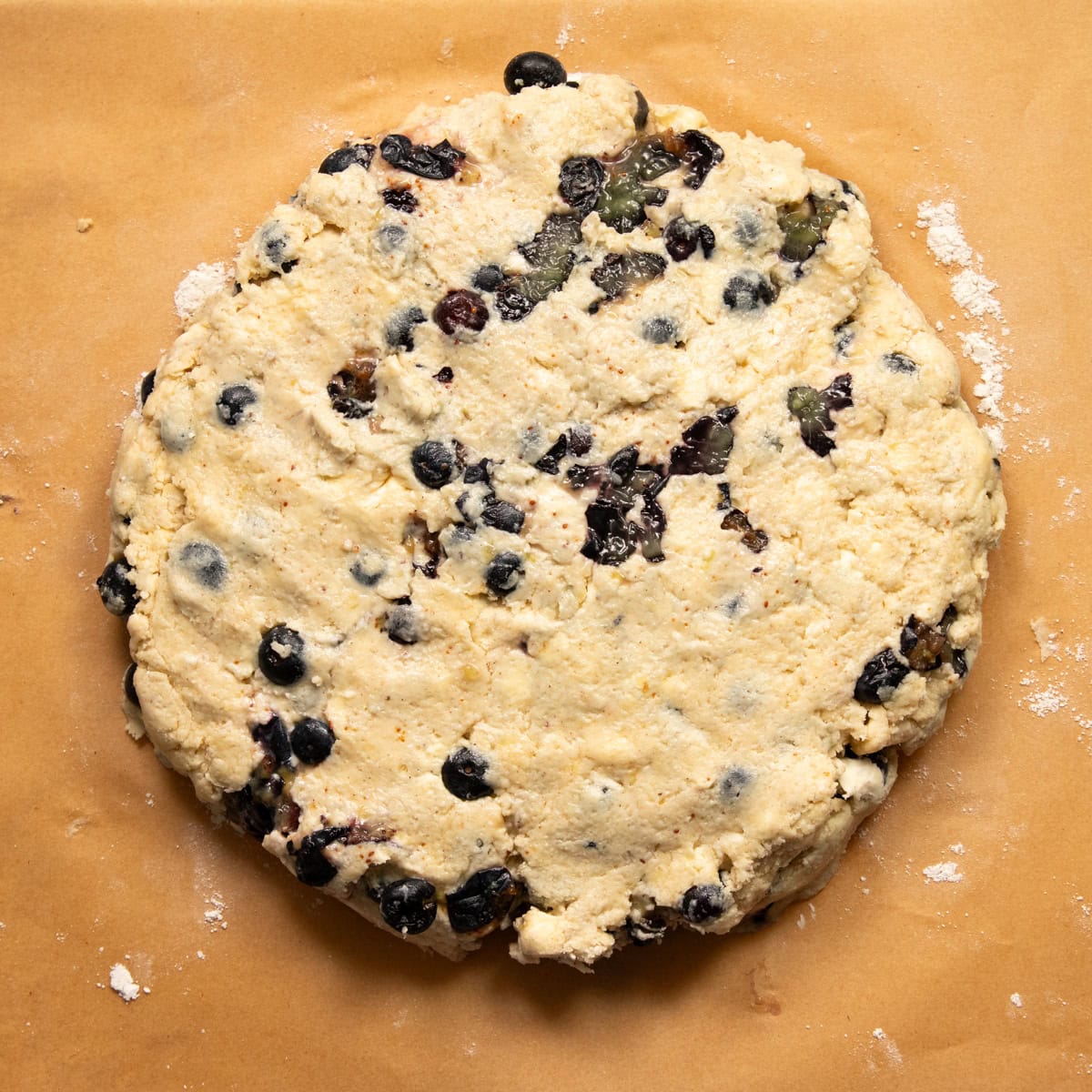 Scone dough is formed into a flat, thick disk on a piece of parchment paper dusted with gluten-free flour.