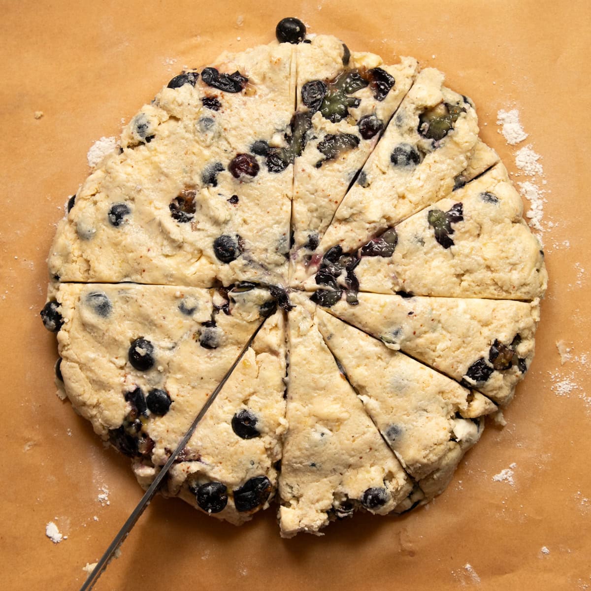 A sharp kitchen knife is slicing a scone dough disk into 12 even pieces.