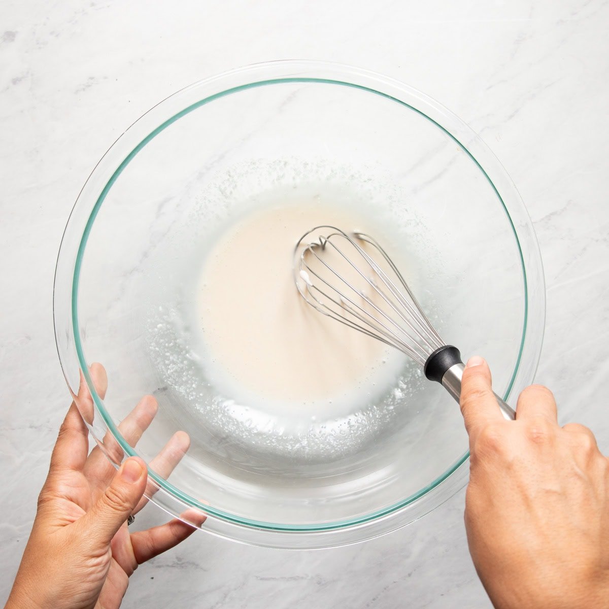 Whisking mayonnaise with sugar and vinegar in a large glass bowl.