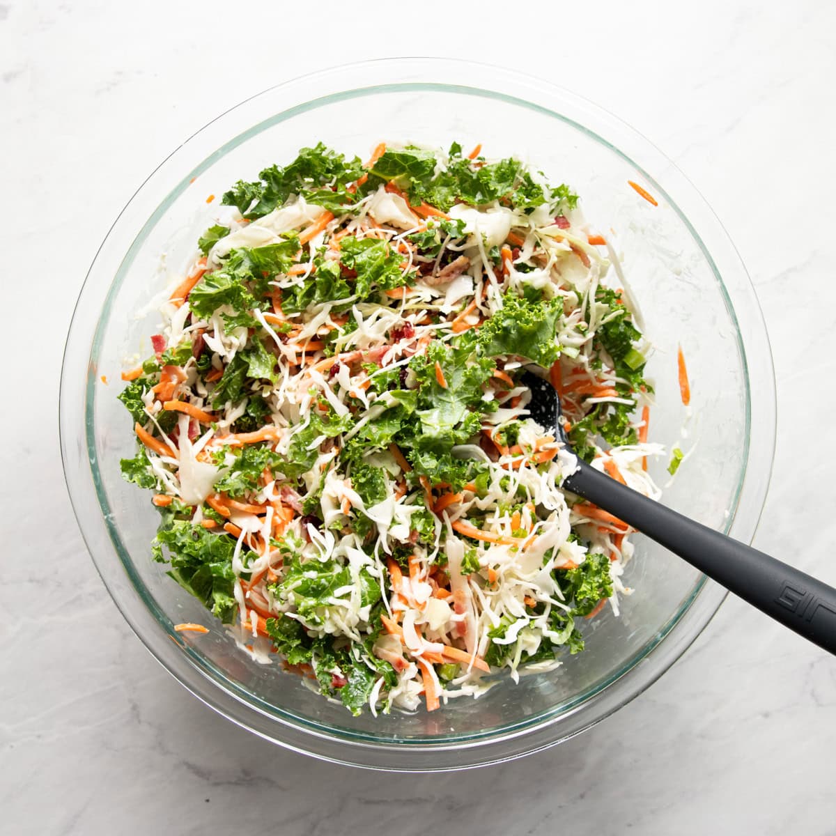 Sunflower crunch salad mixed in a large glass bowl with a scoopula resting in the bowl.