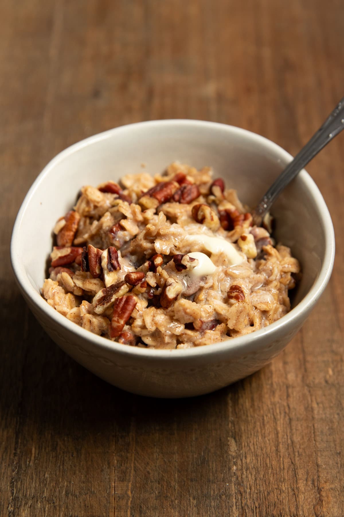 A cozy bowl of oatmeal sitting on a dark wood tray. There's a spoon resting in the bowl waiting for you to take a bite.