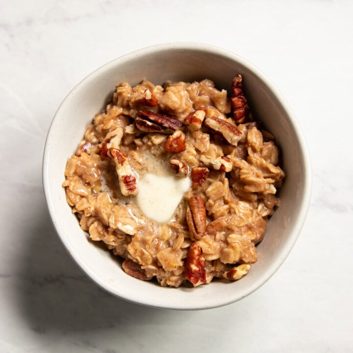 A small bowl of oatmeal topped with chopped pecans and melting butter.