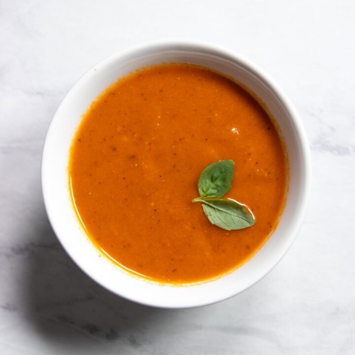 Looking into a small bowl of Low FODMAP Tomato-Basil Soup garnished with two small basil leaves.