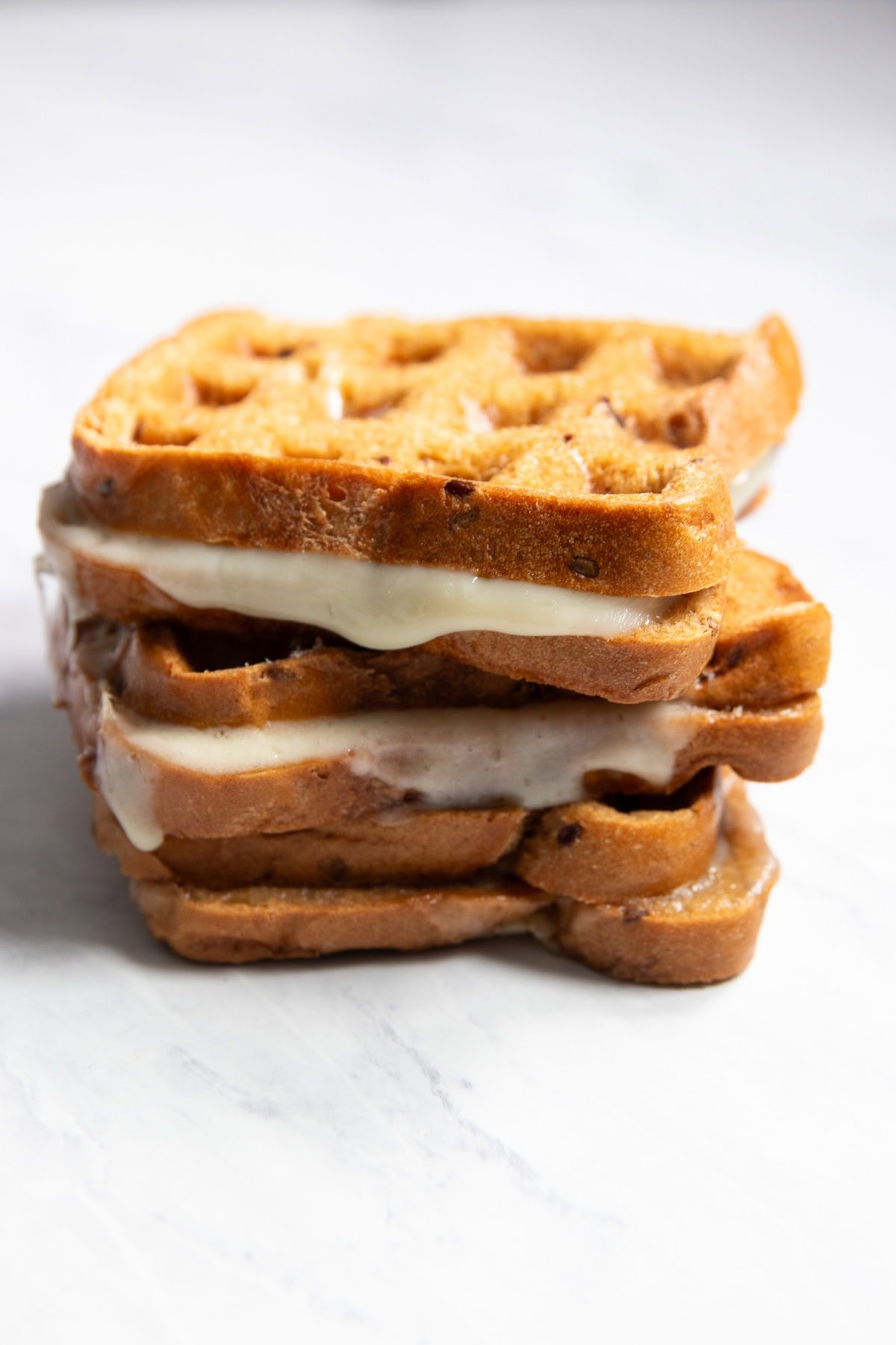 A stack of three waffle maker grilled cheese sandwiches on a white marble counter.