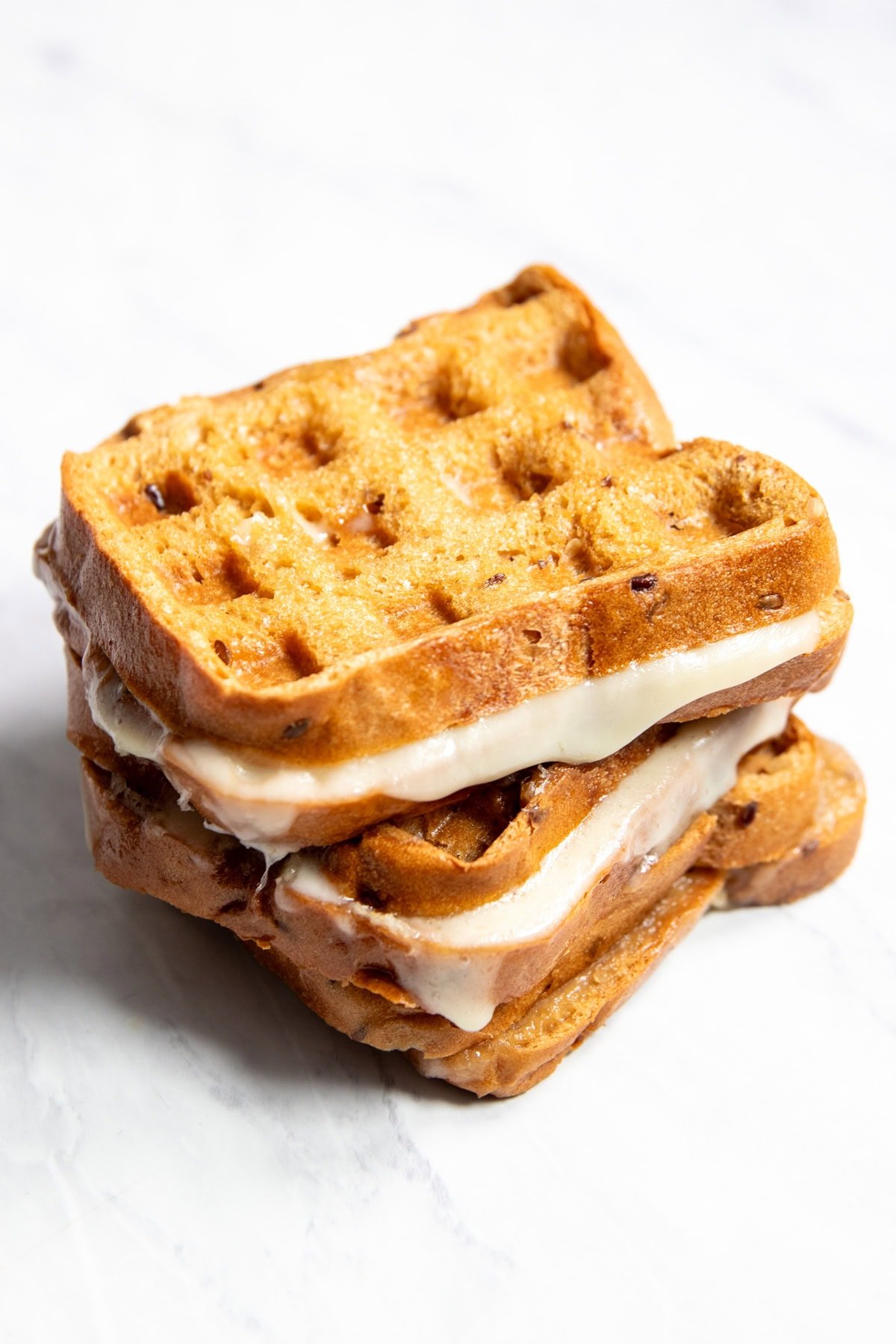 A stack of grilled cheese sandwiches made in a waffle maker are sitting on a white marble counter. 