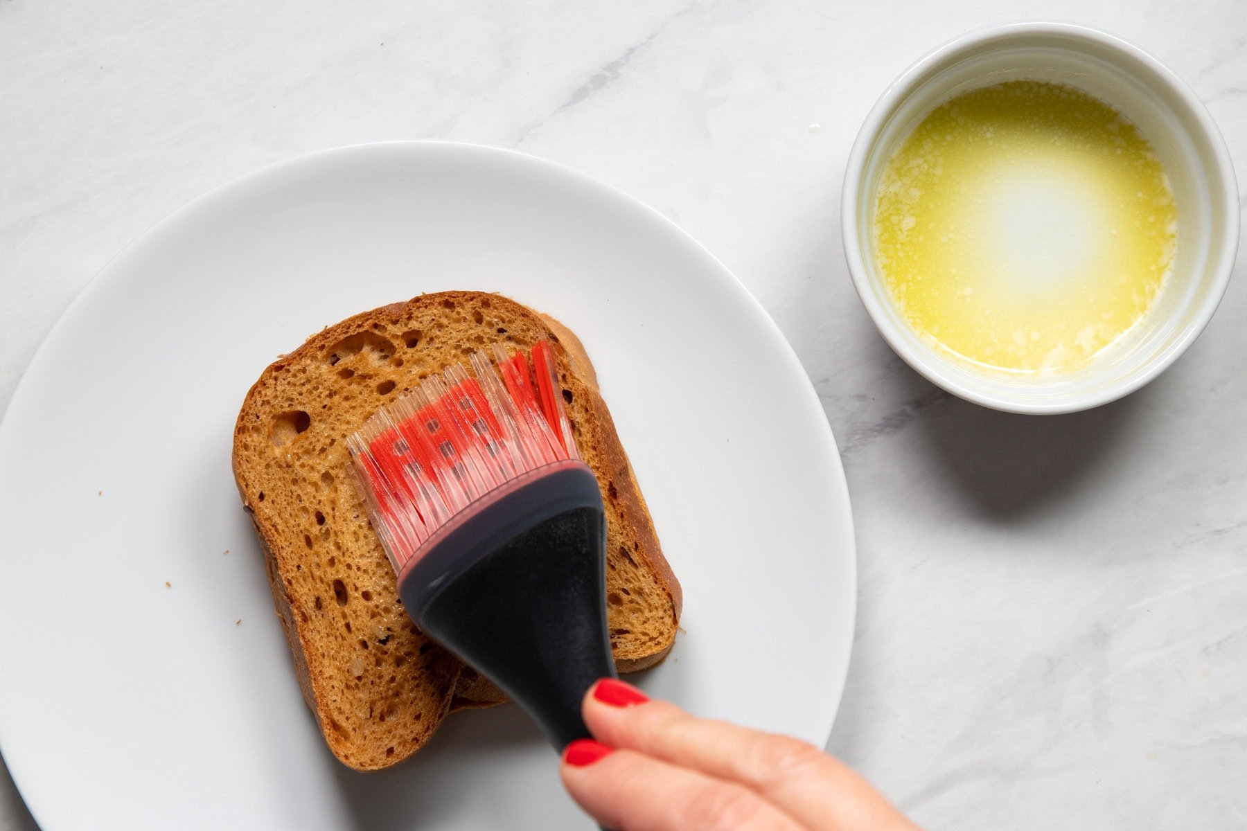 Brushing a piece of low FODMAP bread with melted butter mixed with garlic-infused oil.