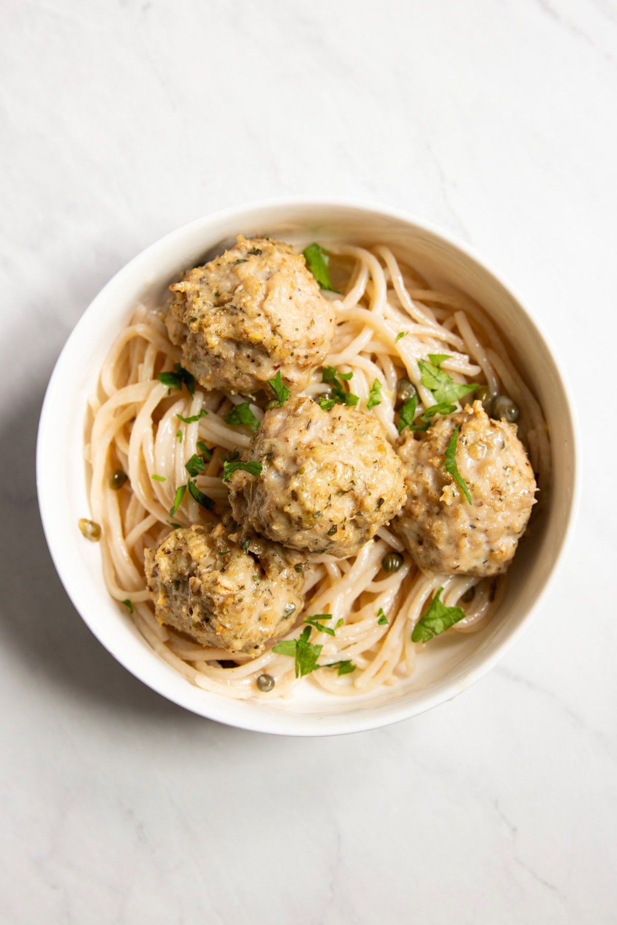 Looking down into a single bowl of chicken piccata meatballs with spaghetti.