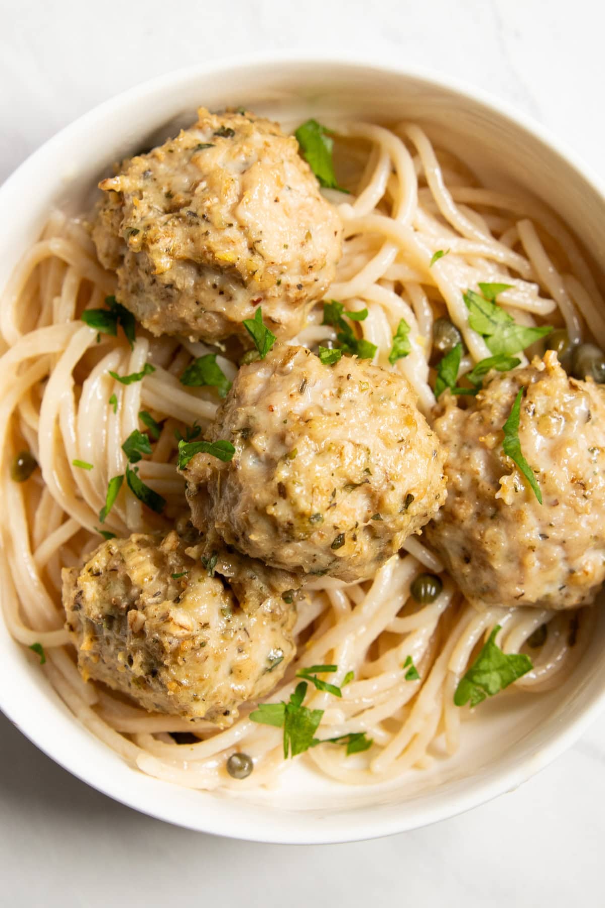 Close up of low FODMAP chicken piccata meatballs on top of gluten-free spaghetti tossed in a lemon-wine-caper sauce.