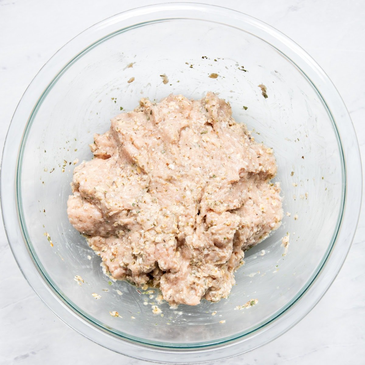 Ground chicken mixed with Italian seasoning, oats, low FODMAP milk, and egg ready to be formed into meatballs.