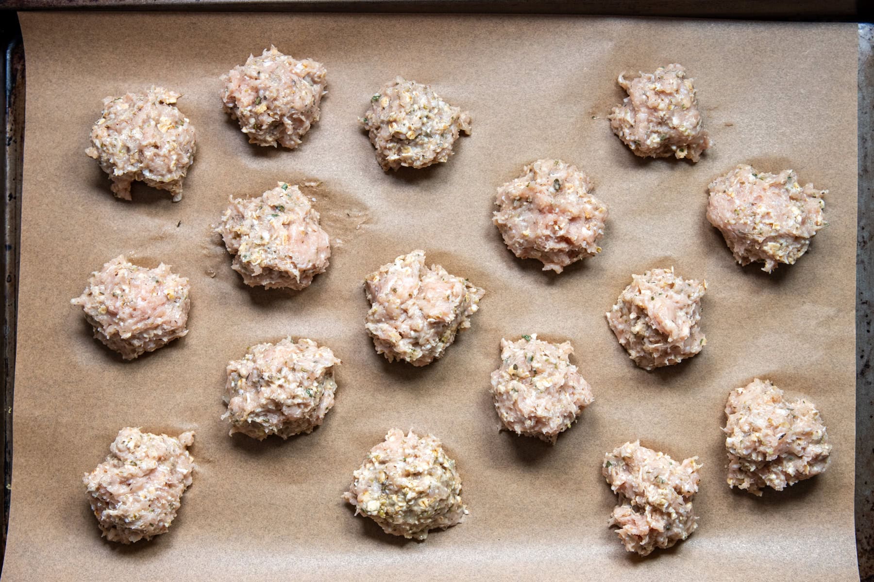 Low FODMAP chicken piccata meatballs are formed and sitting on a parchment-lined baking sheet ready to be baked.