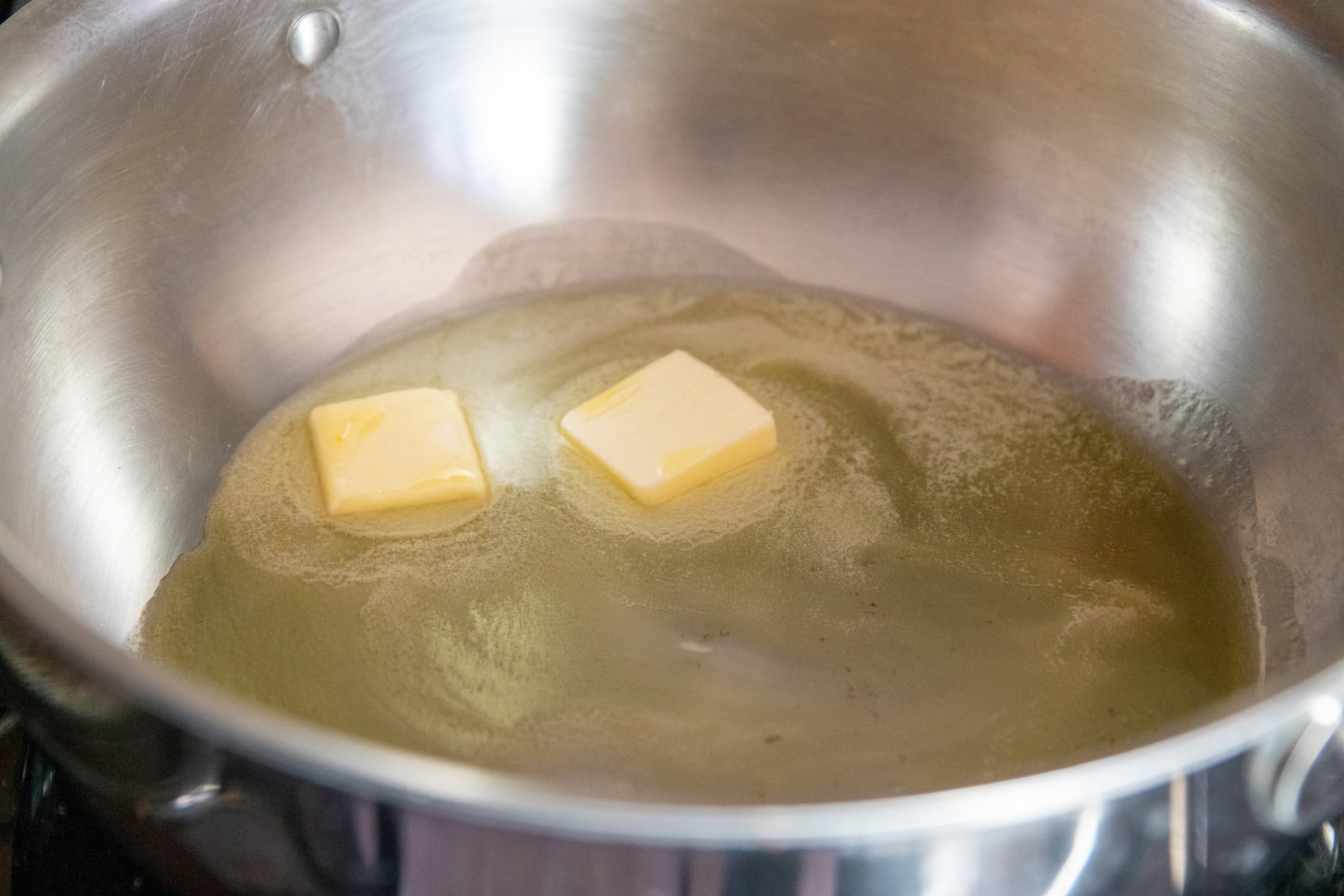 Melting butter with garlic-infused oil in a deep-sided stainless steel skillet.