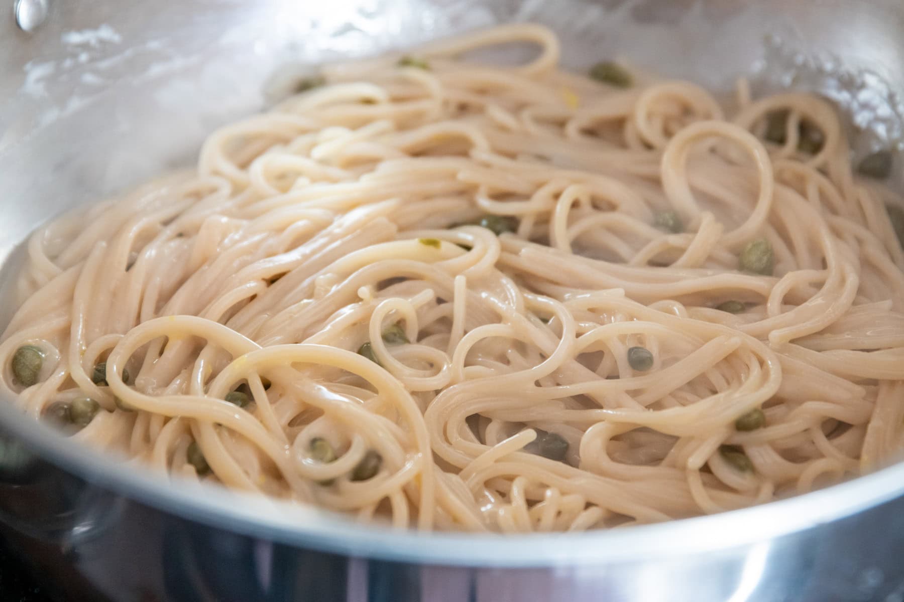 Cooked gluten-free spaghetti is added to the lemon-wine sauce with capers and lemon zest.