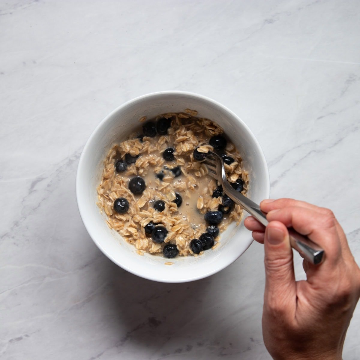 Stirring fresh blueberries into a bowl of almost cooked oatmeal.
