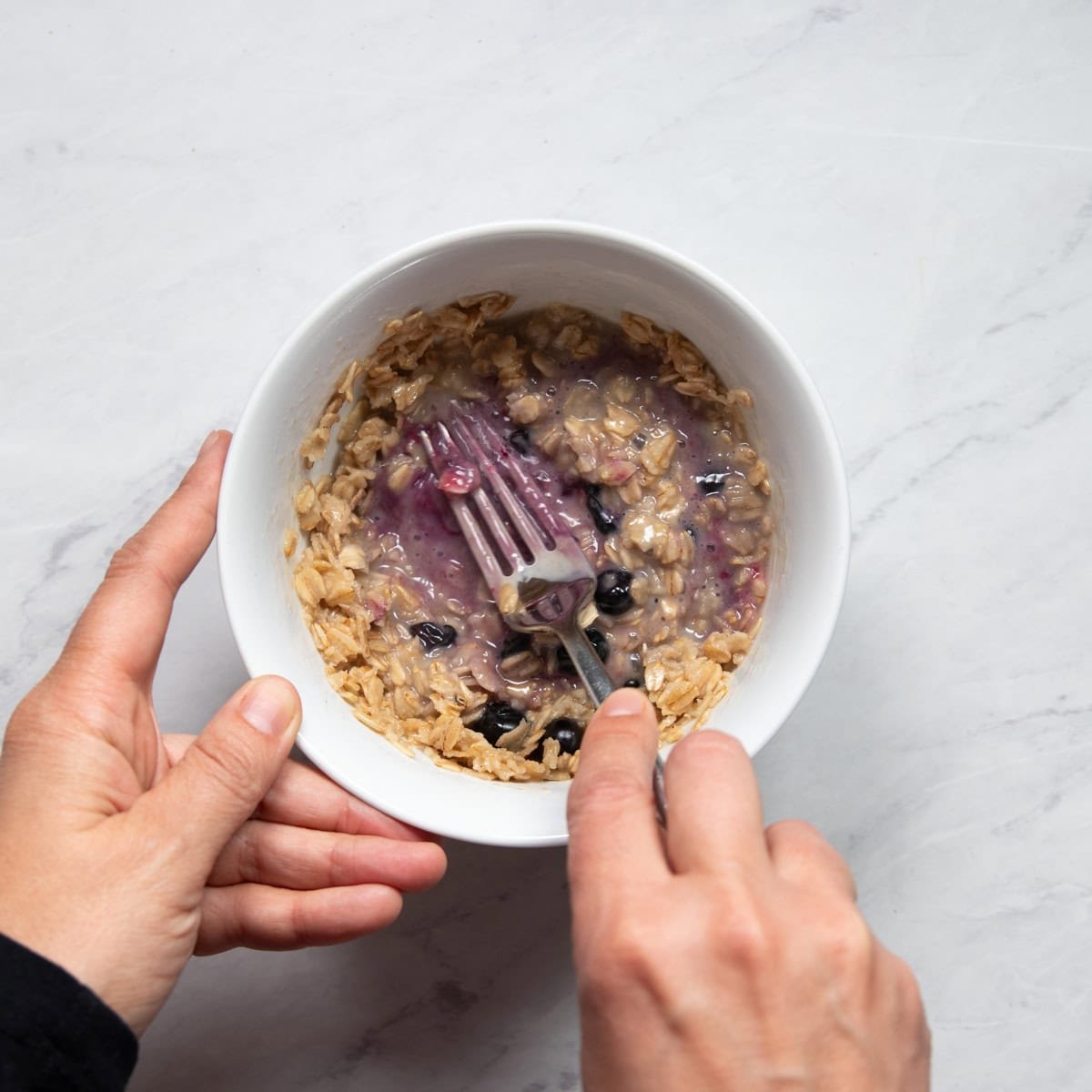 Smashing cooked blueberries into oatmeal with a fork. 