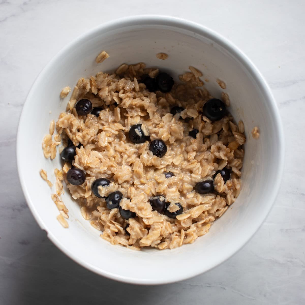 A bowl of cooked oatmeal made with fresh blueberries. The oatmeal looks bright brown because the blueberries are largely intact after cooking.