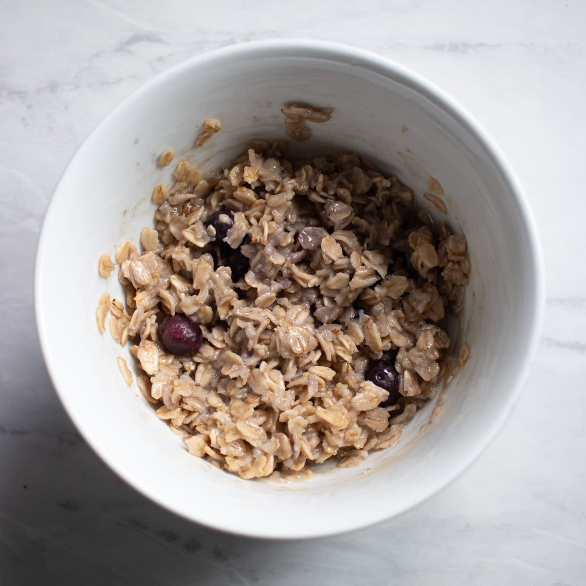 Cooked oatmeal made with frozen blueberries. The oatmeal is a dull brown with a slight purple-blue tint because the frozen blueberries have bled a bit during cooking.  