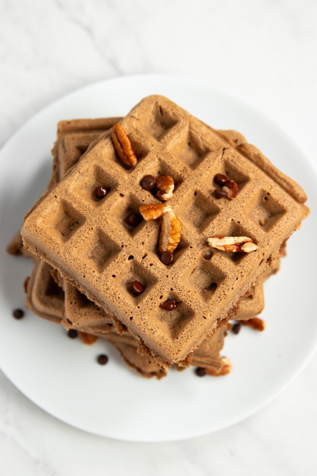 Looking down onto a stack of chocolate waffles topped with chopped pecans and mini chocolate chips.
