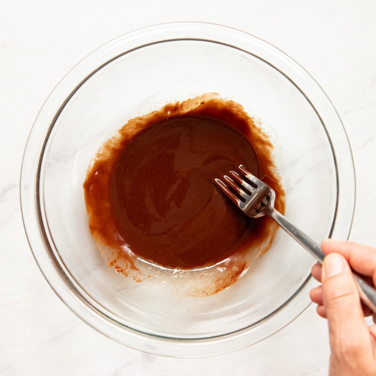 Stirring melted chocolate chips and butter in a large glass bowl with a fork.