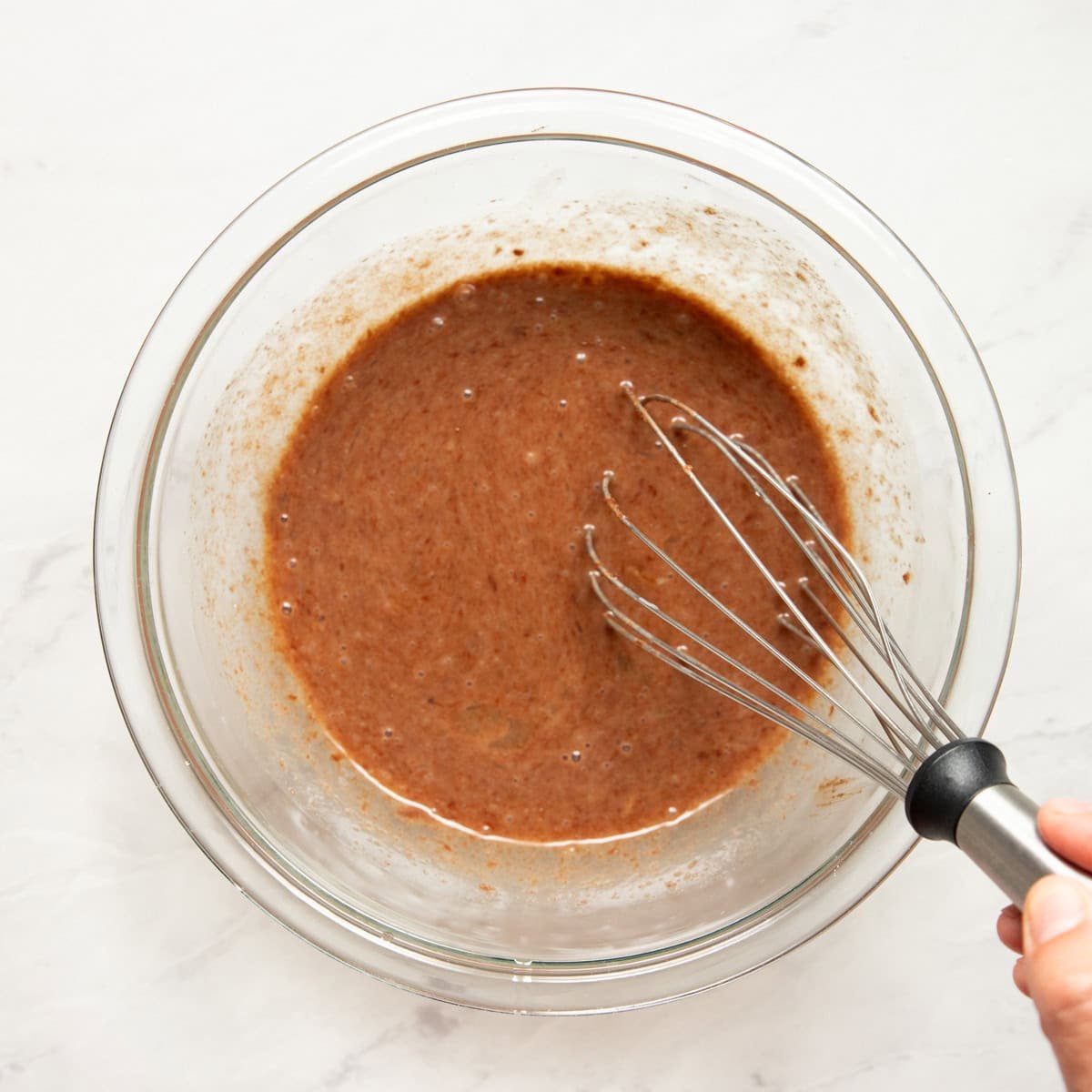 Whisking low FODMAP milk and eggs into a melted chocolate-butter-sugar mixture.