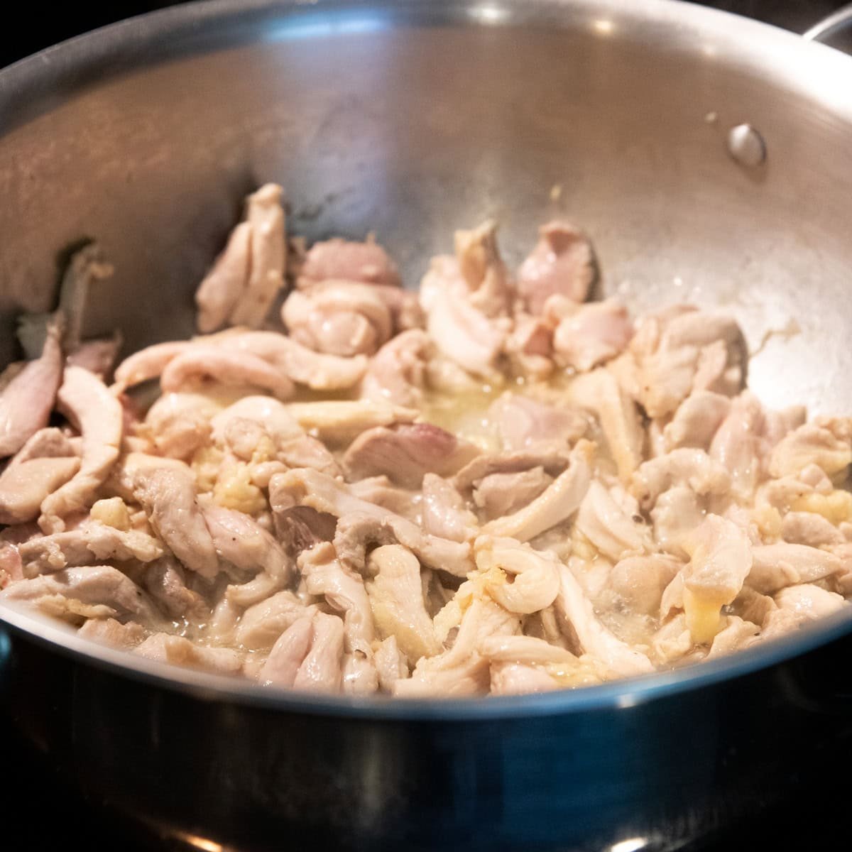 Chicken thigh strips are cooking in a stainless steel skillet.