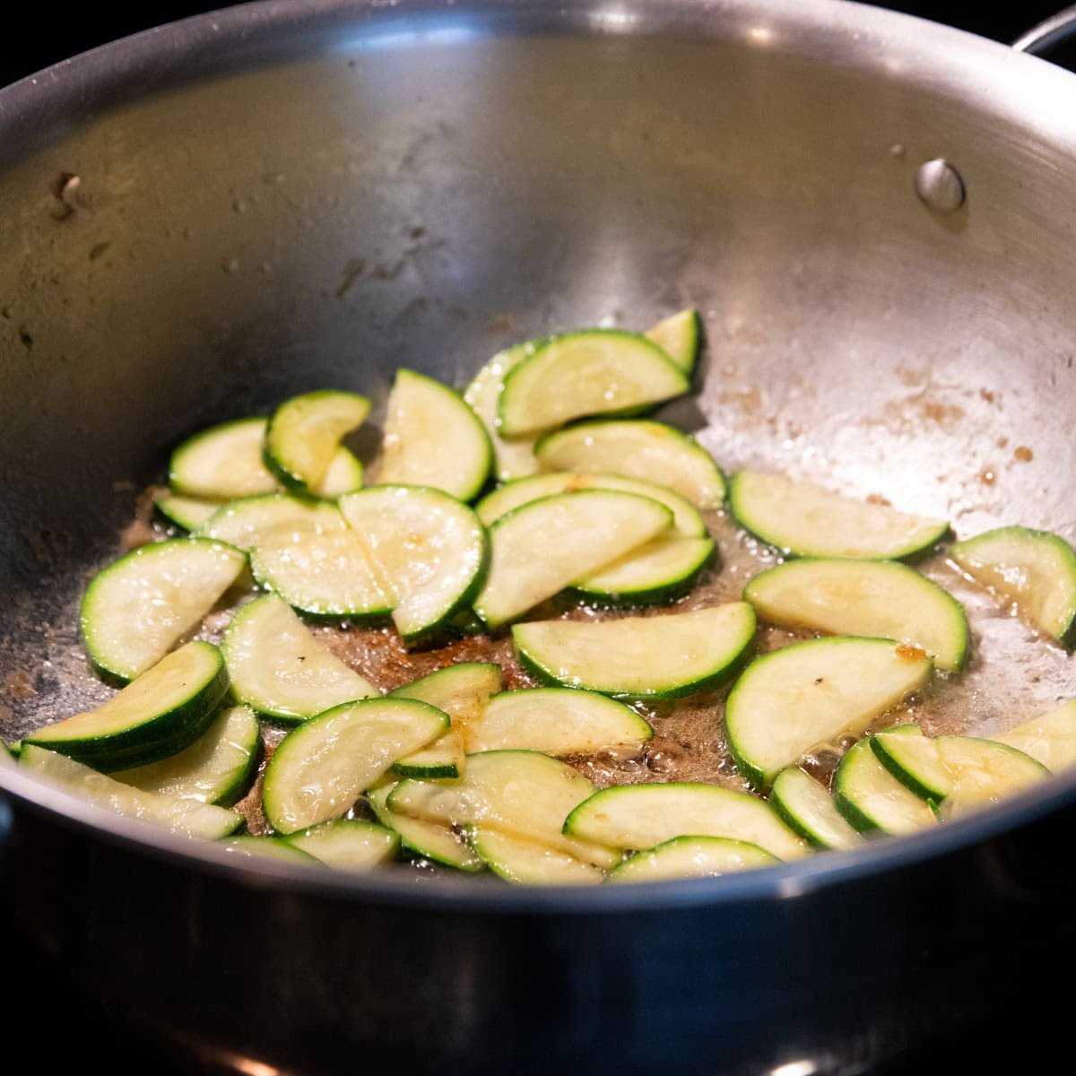 Zucchini sliced into half moons sauteing in a skillet