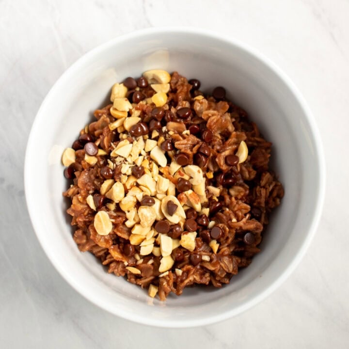 Looking down into a bowl of chocolatey oatmeal topped with chopped peanuts and mini chocolate chips.