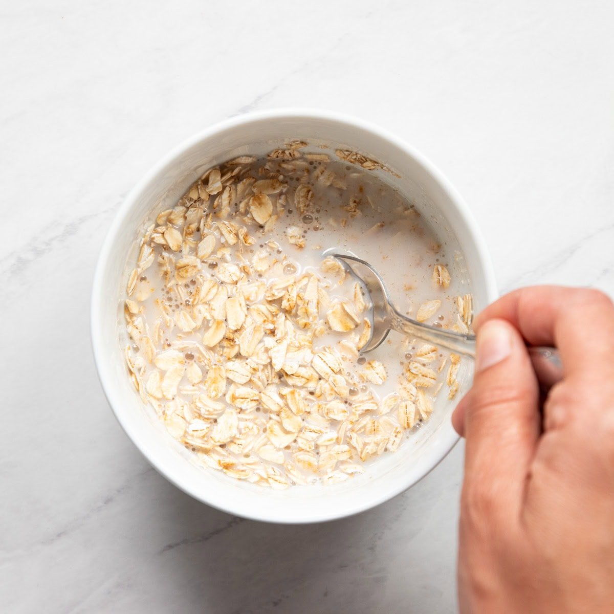 Stirring low FODMAP milk into a bowl of uncooked rolled oats.