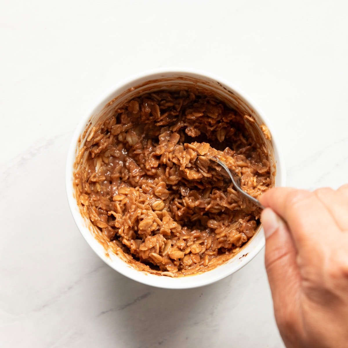 Stirring cocoa powder and peanut butter into a bowl of cooked rolled oats.