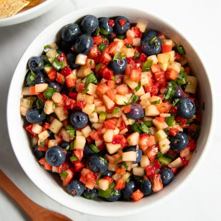 Looking down at a bowl of fruit salsa. There's a small wooden spoon and bowl of tortilla chips peeking in the left corners of the frame.