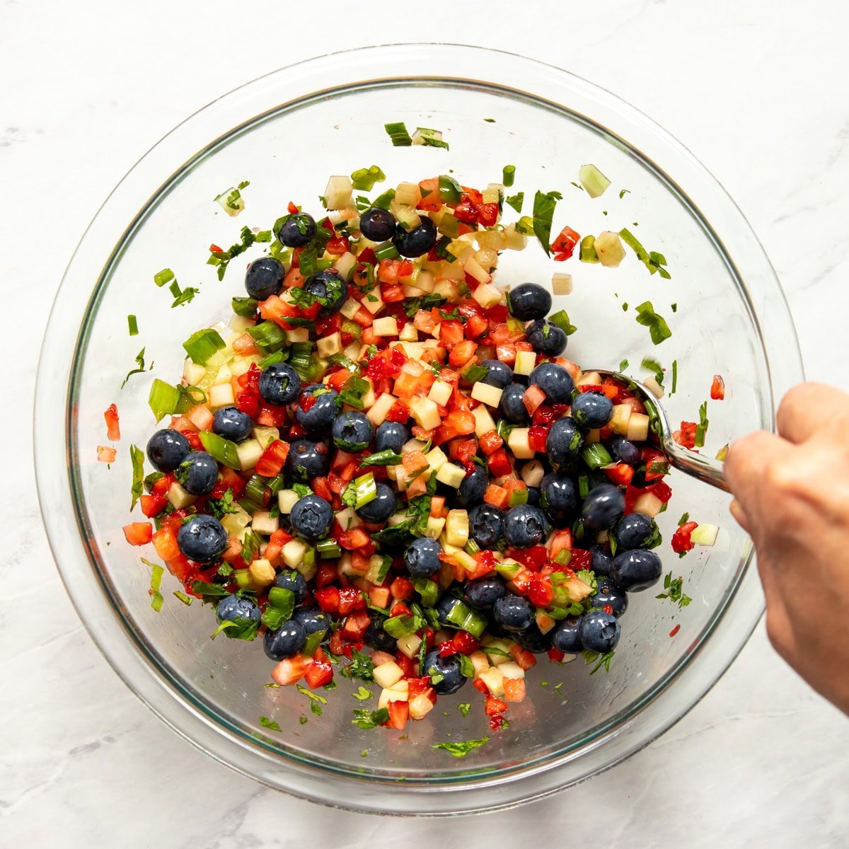 Mixing the low FODMAP fruit salsa components in a large glass mixing bowl with a spoon.