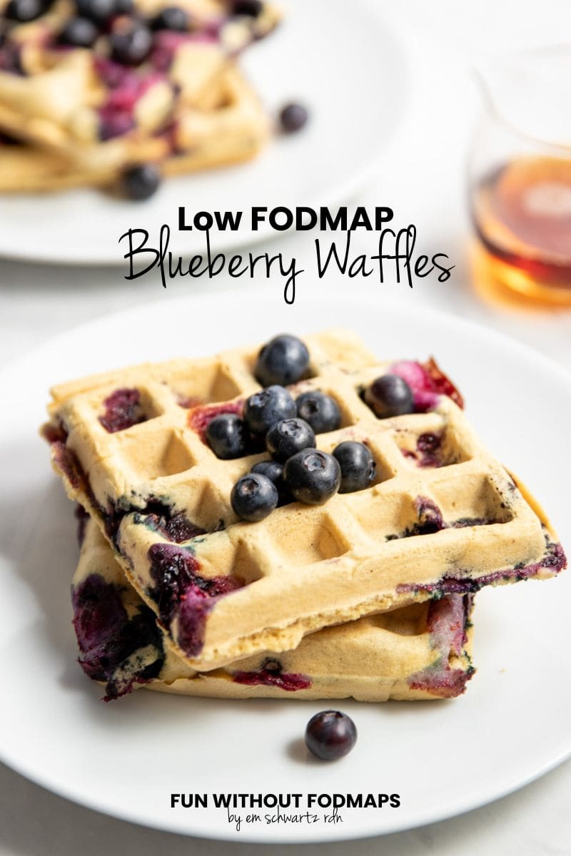 Plates of blueberry waffles are staggered on a countertop with a small glass container of maple syrup. In the white space, black text reads "Low FODMAP Blueberry Waffles."