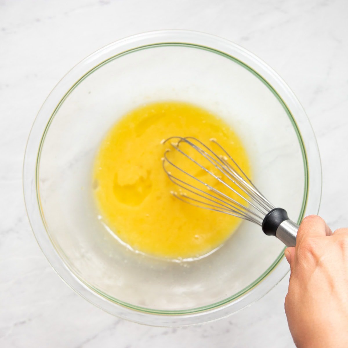 Whisking melted butter with sugar, low FODMAP milk, and eggs in a large glass mixing bowl.
