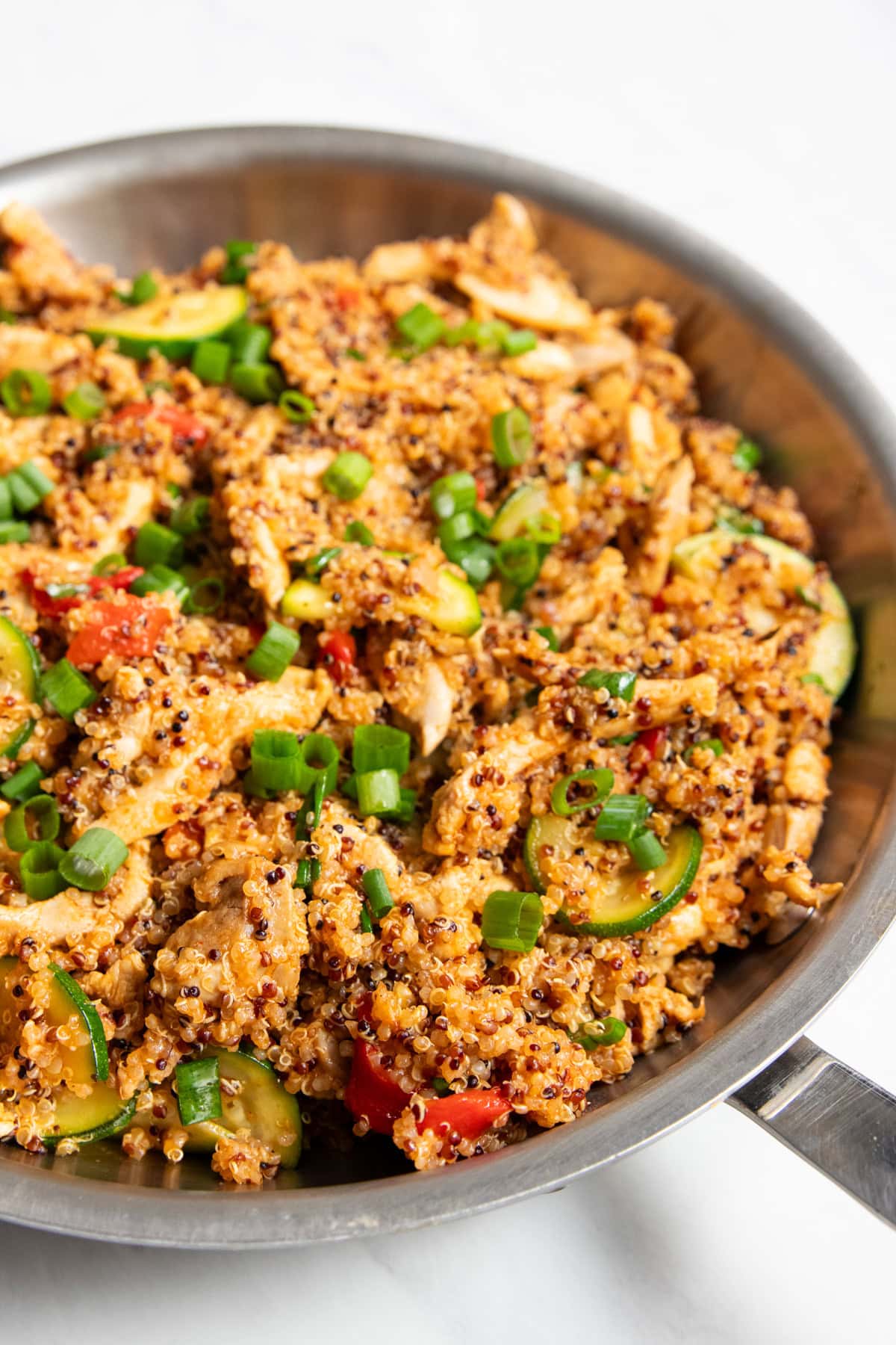 A skillet filled with cooked quinoa, chicken, and veggies sitting on a white marble counter.