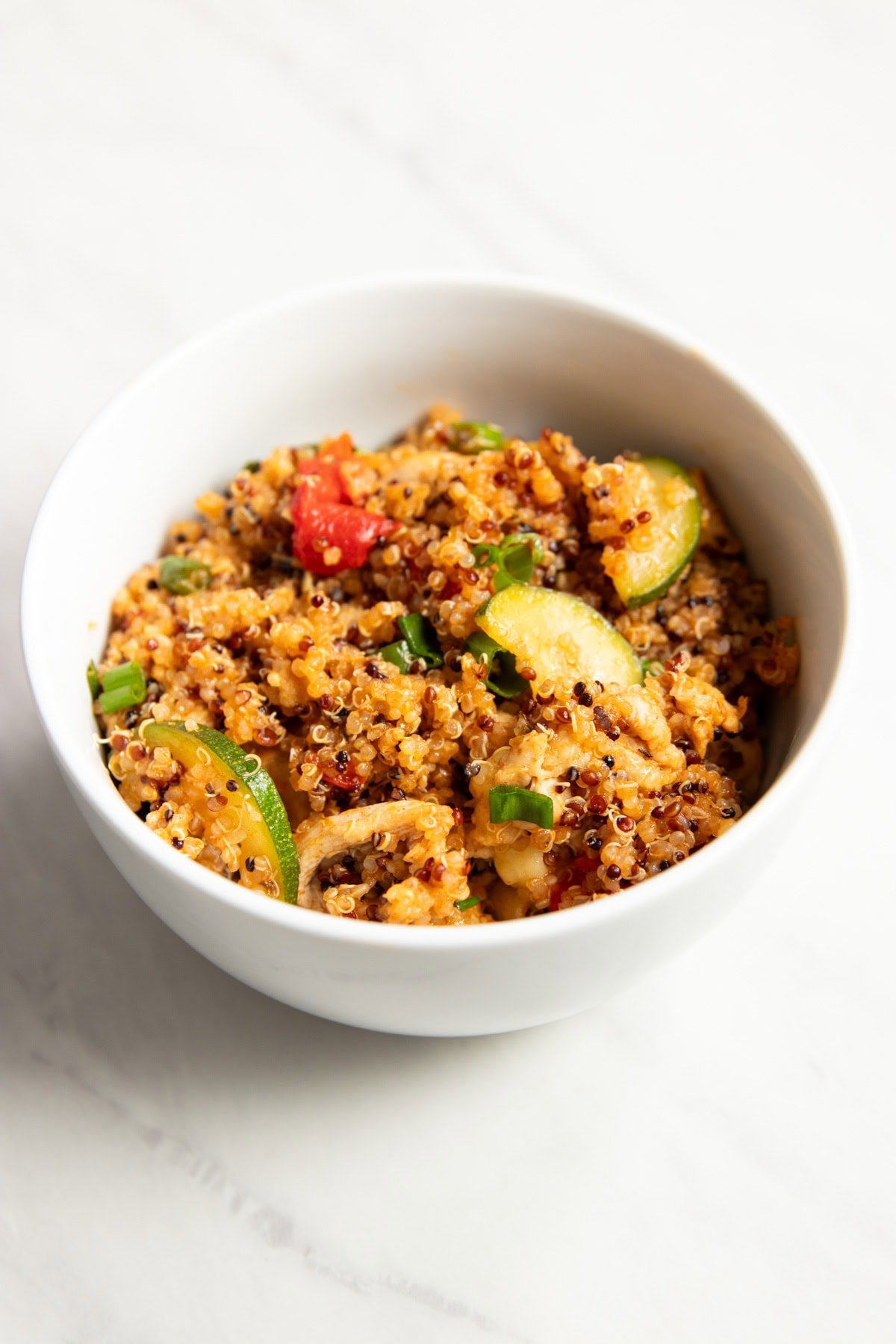 A single white bowl filled with Low FODMAP Cajun Chicken with Quinoa and Veggies.