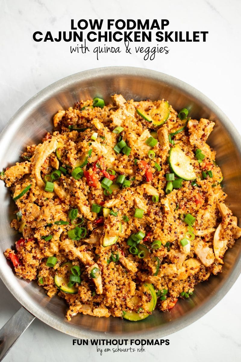 A stainless steel skillet filled with chicken strips, whole grain quinoa, roasted red peppers, zucchini, and green onion tops. In the white space above, black text reads "Low FODMAP Cajun Chicken Skillet with Quinoa and Veggies."