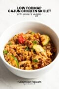 A bowl of a chicken-quinoa-veggie main dish sitting on a white counter. In the white space above, black text reads "Low FODMAP Cajun Chicken Skillet with Quinoa and Veggies."