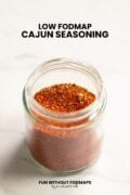 Looking at a small glass jar filled with a spice mix sitting on a counter. In the white space above, black text reads "Low FODMAP Cajun Seasoning."