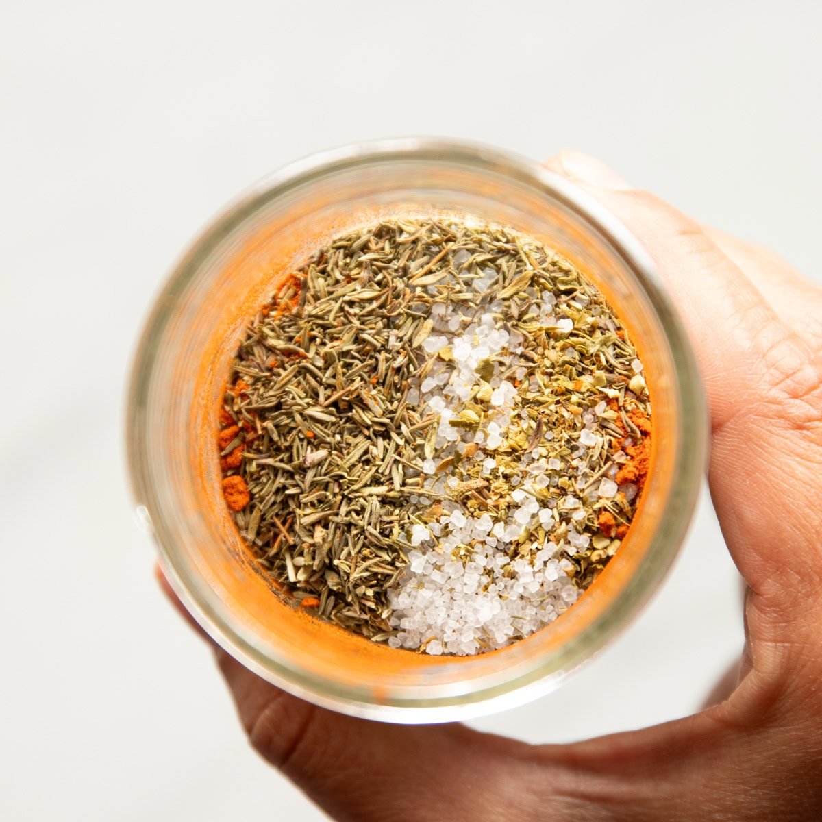A hand holding a jar of spices ready to be sealed and shaken.