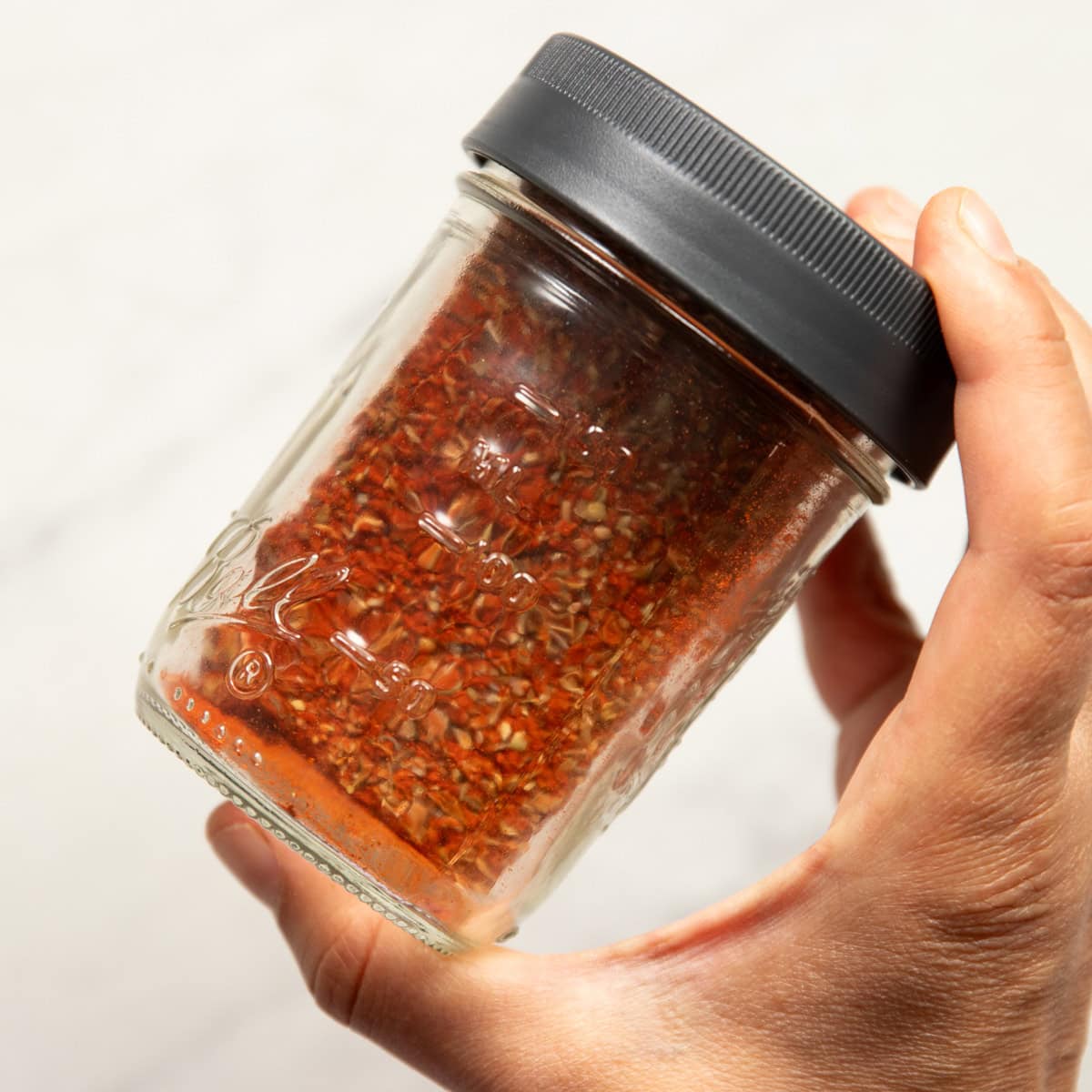 A hand is holding a sealed mason jar containing a spice blend that has just been shaken. 
