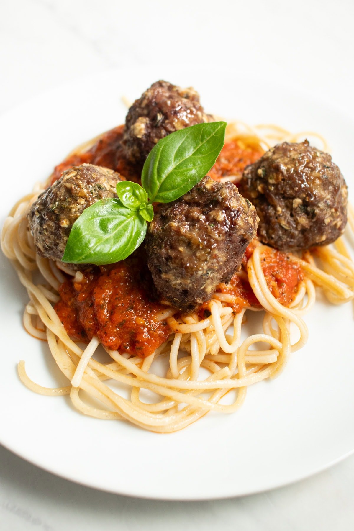 A plate of beef meatballs sitting on top of a bed of spaghetti with tomato sauce. 