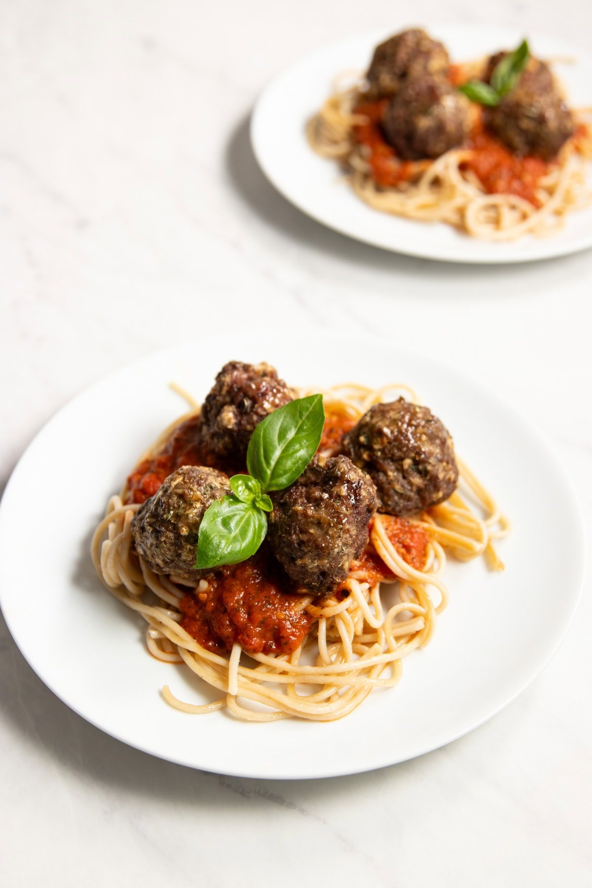 Two plates of low FODMAP spaghetti and meatballs on a white marble counter.